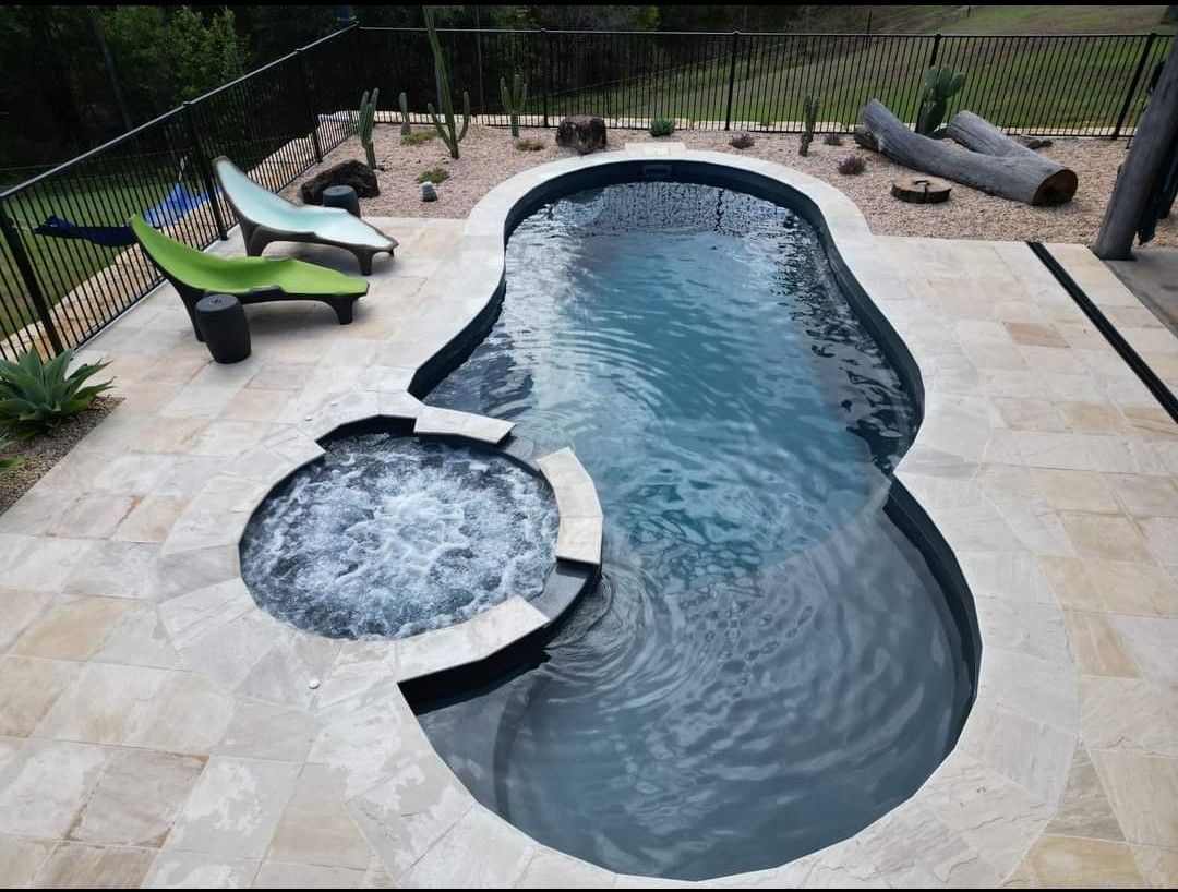 Curved pool with attached hot tub on stone patio surrounded by desert landscape